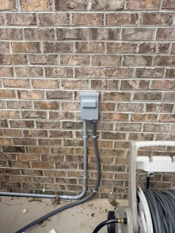 Covered exterior electrical outlet and conduit mounted on a brick wall