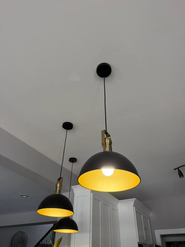 Close view of a lit black pendant shade with a gold interior and brass fitting