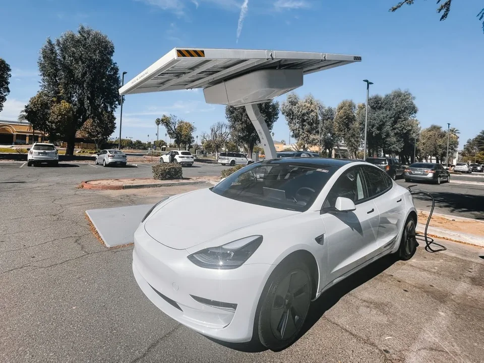 White electric car connected to a charging station under a solar canopy.