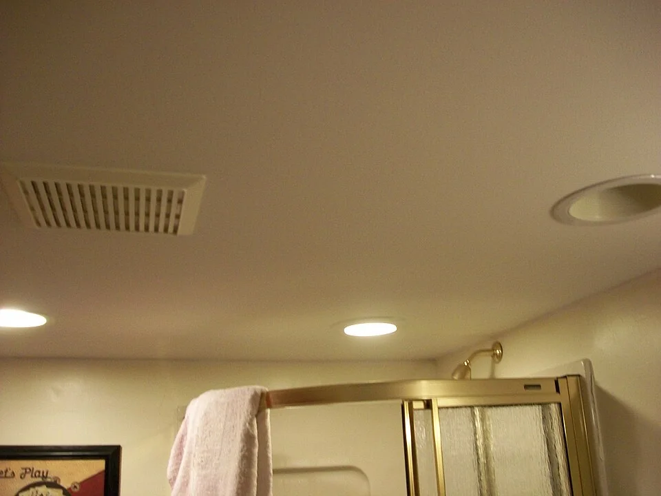 Rectangular bathroom ceiling exhaust grille beside recessed lights.