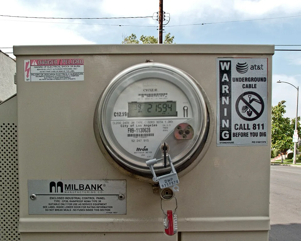 Digital utility electricity meter mounted in a metal meter enclosure.