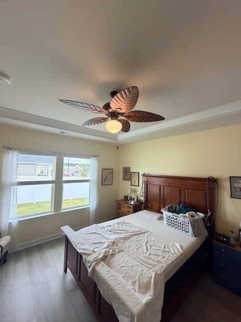 A brighter bedroom. A leaf-blade ceiling fan with its light illuminated in a bedroom.