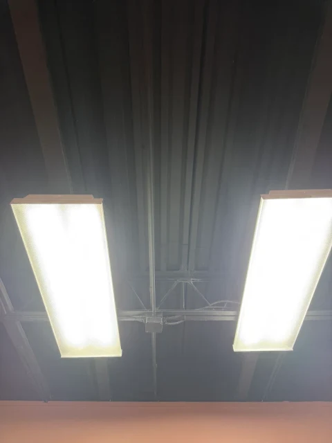 Light for the workspace. Two illuminated ceiling fixtures beneath an exposed commercial ceiling.