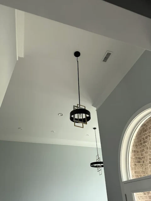 Fixtures in a tall entry. Two pendant fixtures suspended in a tall entryway beside an arched window.