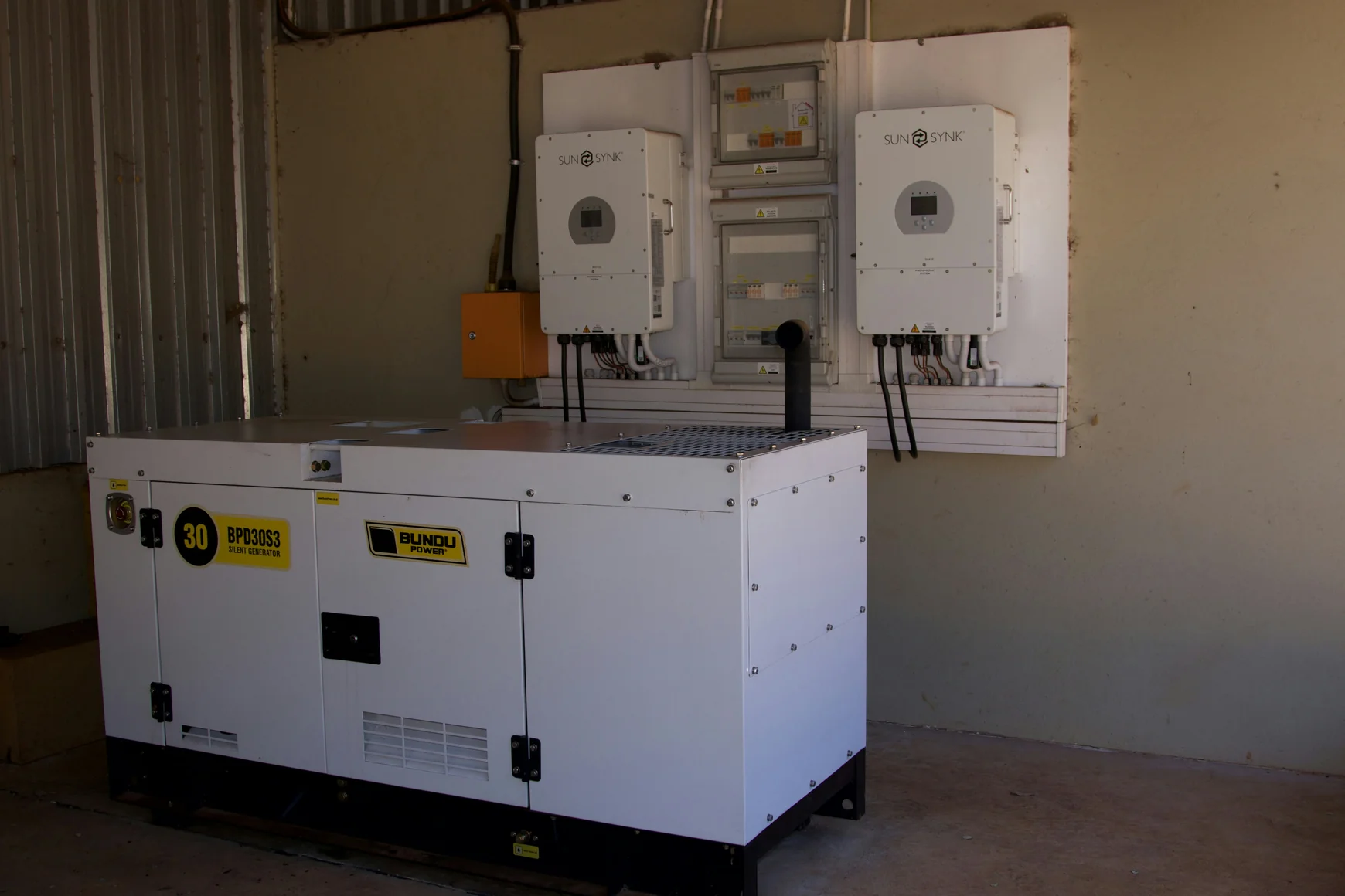 A large white generator next to wall-mounted power inverters — stock photograph